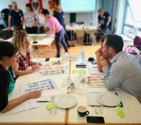 Vier Menschen sitzen an einem Tisch und überlegen, am Tisch liegen Unterlagen und Informationsblätter