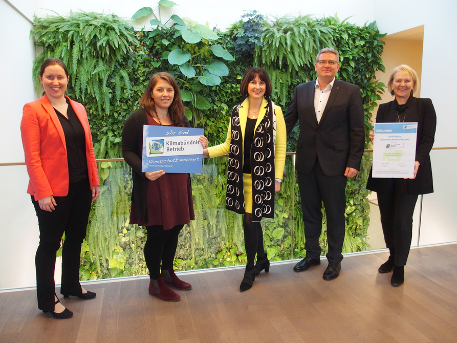 5 Personen stehen vor einer begrünten Wand und halten zwei Klimabündnis-Tafeln.