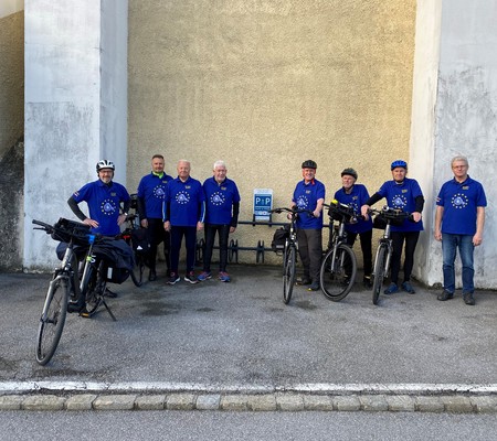 Eine Gruppe blau gekleideter Männer und Frauen stehen vor einer Kirche bei einem Fahrradabstellplatz.