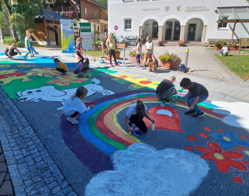 Kinder bemalen einen autofreien Straßenabschnitt mit bunten Farben, Tieren und einem Regenbogen.
