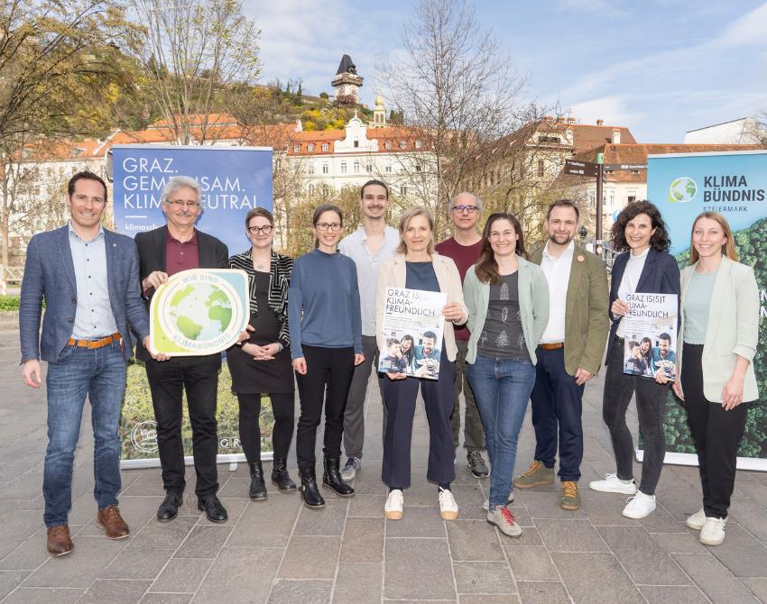 Gruppenbild auf dem gepflasterten Vorplatz vor dem Lendhafen. Im Hintergrund ist der Schlossberg mit Uhrturm sichtbar.