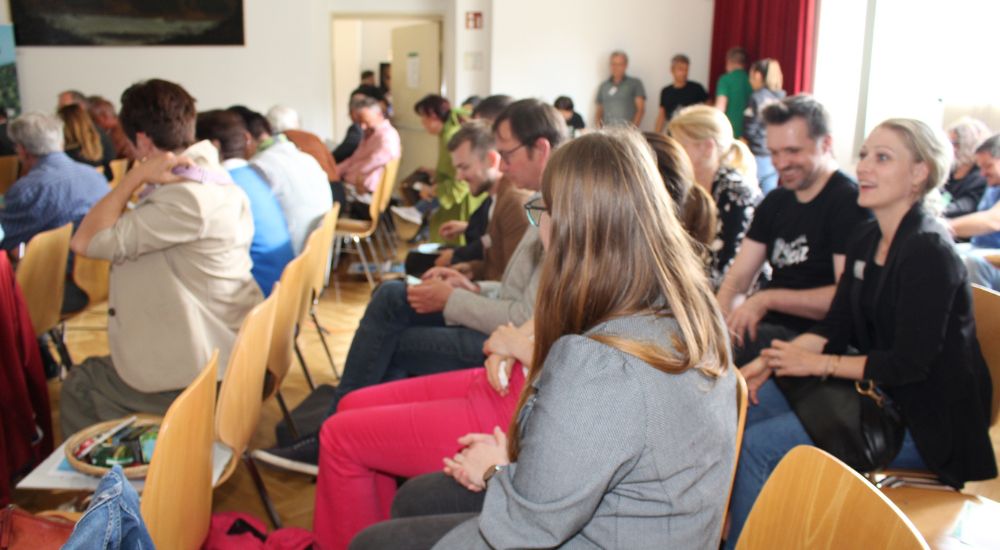 Personen sitzen auf Stühlen und schauen auf die Vortragende und die Leinwand