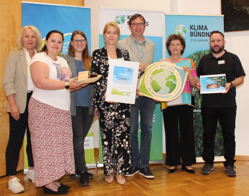 Gruppenbild mit 7 Personen vor Roll-Ups. Eine Person hat eine Klimabündnis-Tafel in der Hand, eine weitere eine Urkunde für die Europäische Mobilitätswoche 2023