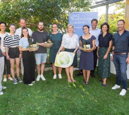 Gruppenbild, 3 Personen halten Körbe mit Lebenmitteln, im Hintergrund ein Roll-Up vom Klimaschutz Graz, im Vordergrund eine Holztafel "Wir sind Klimabündnis"