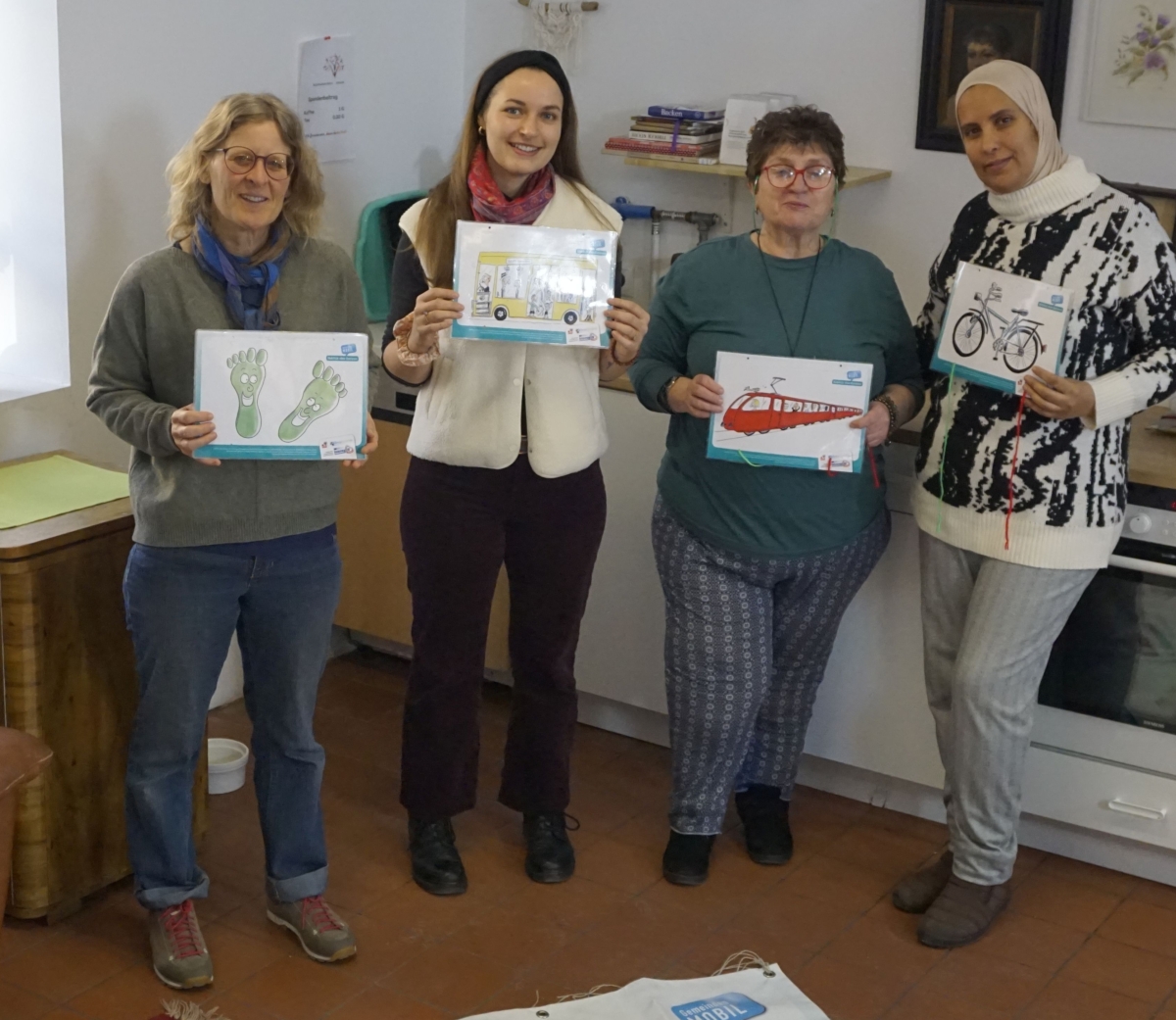 Vier Frauen mit Bildern von Verkehrsmitteln in der Hand stehen vor Plakat, das am Boden liegt