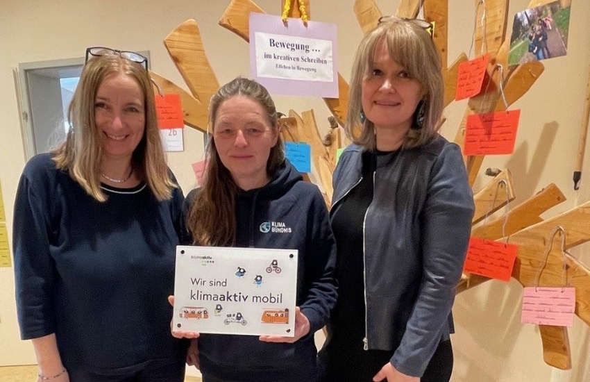 drei Frauen mittleren alters halten ein klimaaktiv Schild hoch und lachen in die Kamera