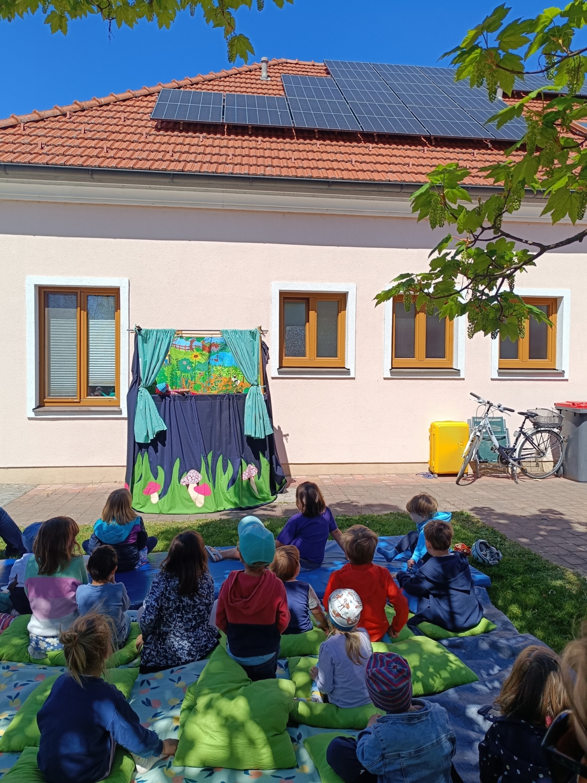 Kinder sitzen vor den Kasperltheater auf der Wiese.